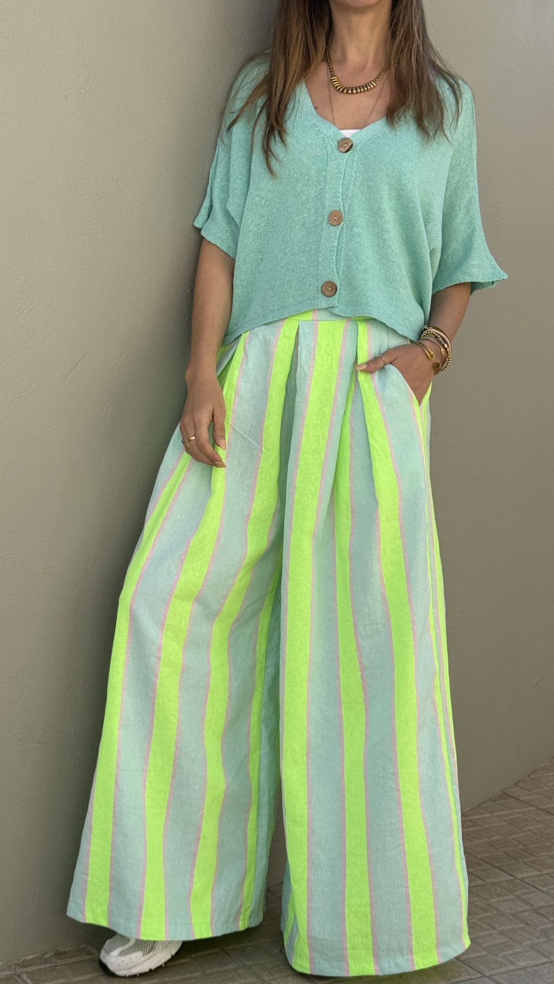 Mulher de camisola verde pastel e calças largas às riscas com ténis blancos