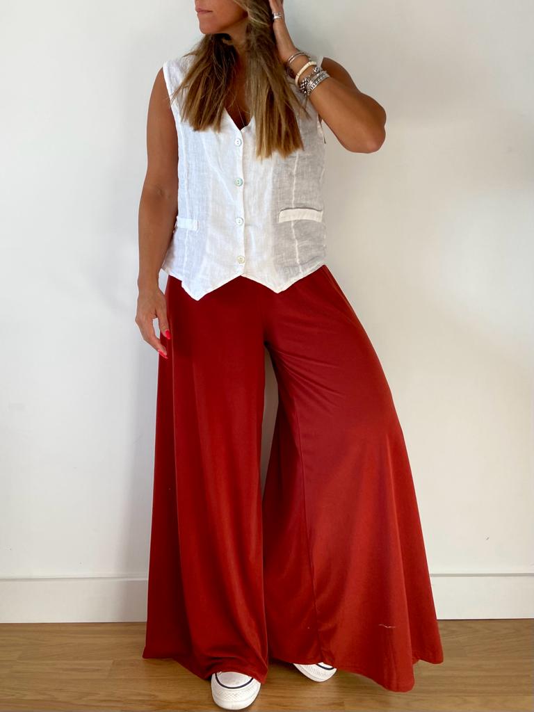 Mulher com colete branco e calças largas vermelhas em fundo branco