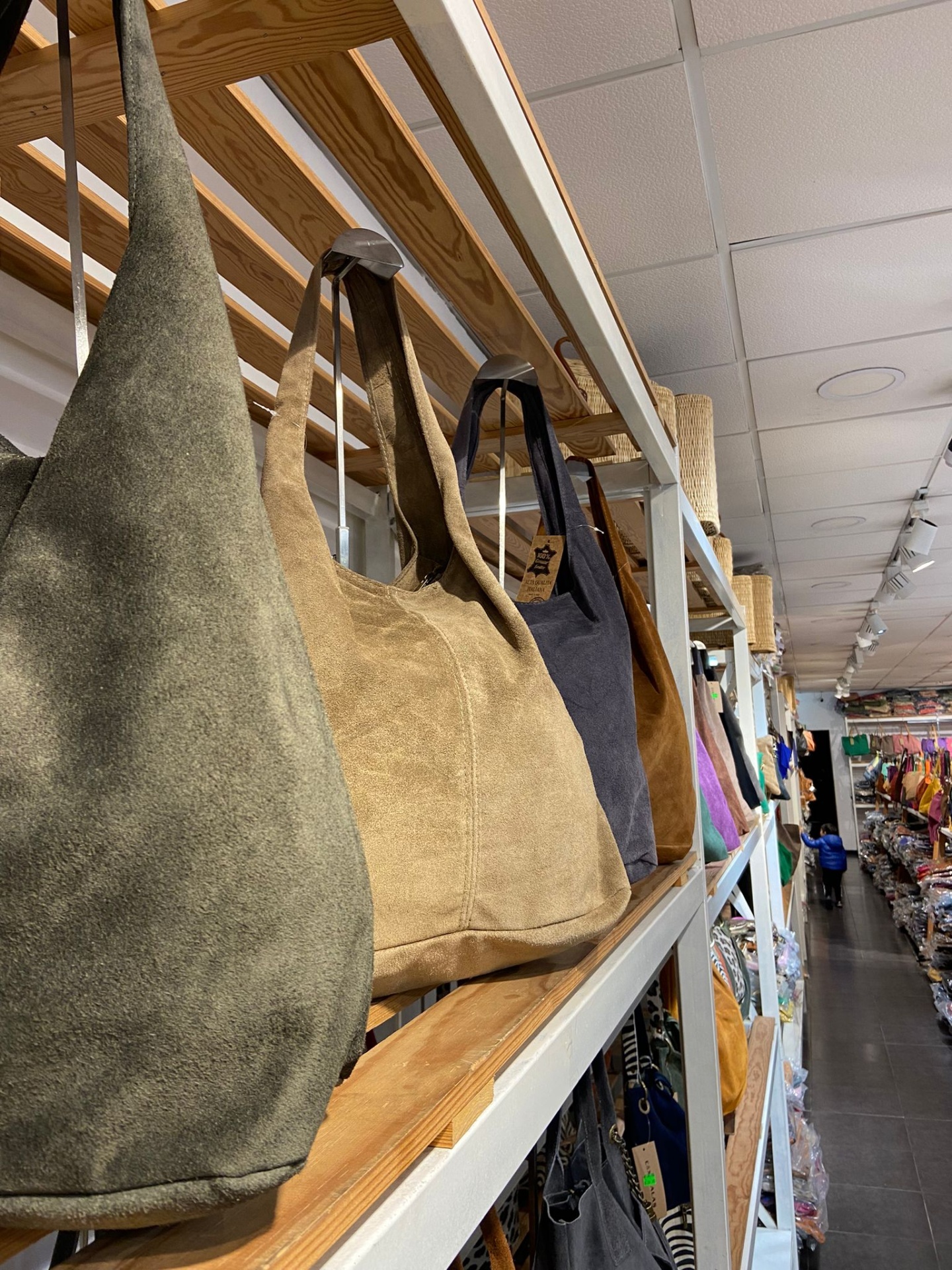 Sacos de tecido em verde, bege e cinza em prateleiras de madeira numa loja