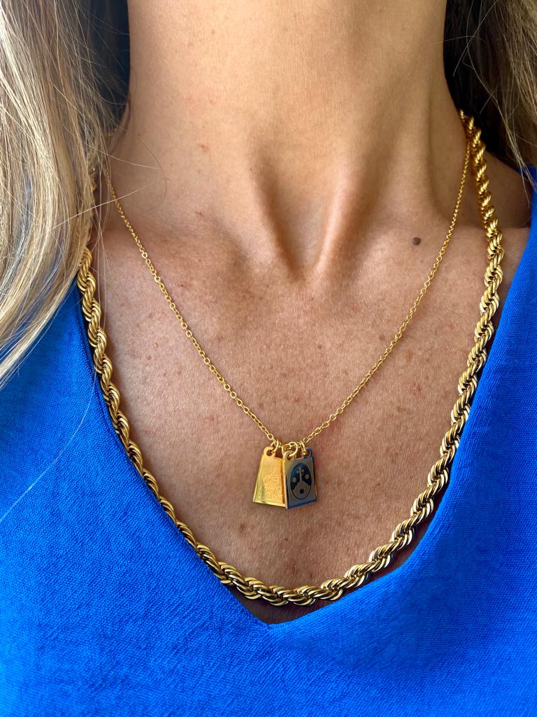 Colar dourado com dois pingentes pendurados em pescoço de pessoa com camisa azul