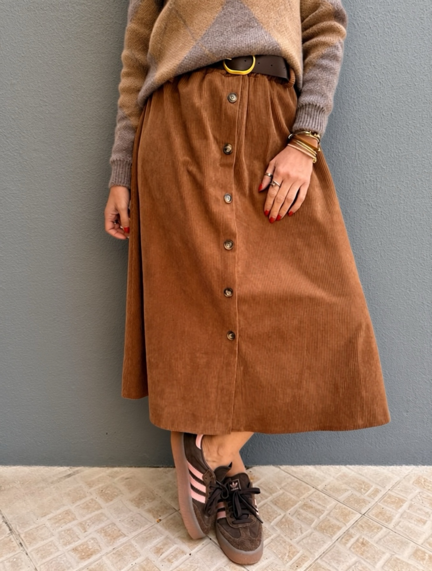 Saia midi castanha de veludo cotelê com botões frontais usada com cinto castanho e sapatos desportivos castanho escuros com riscas rosa claro