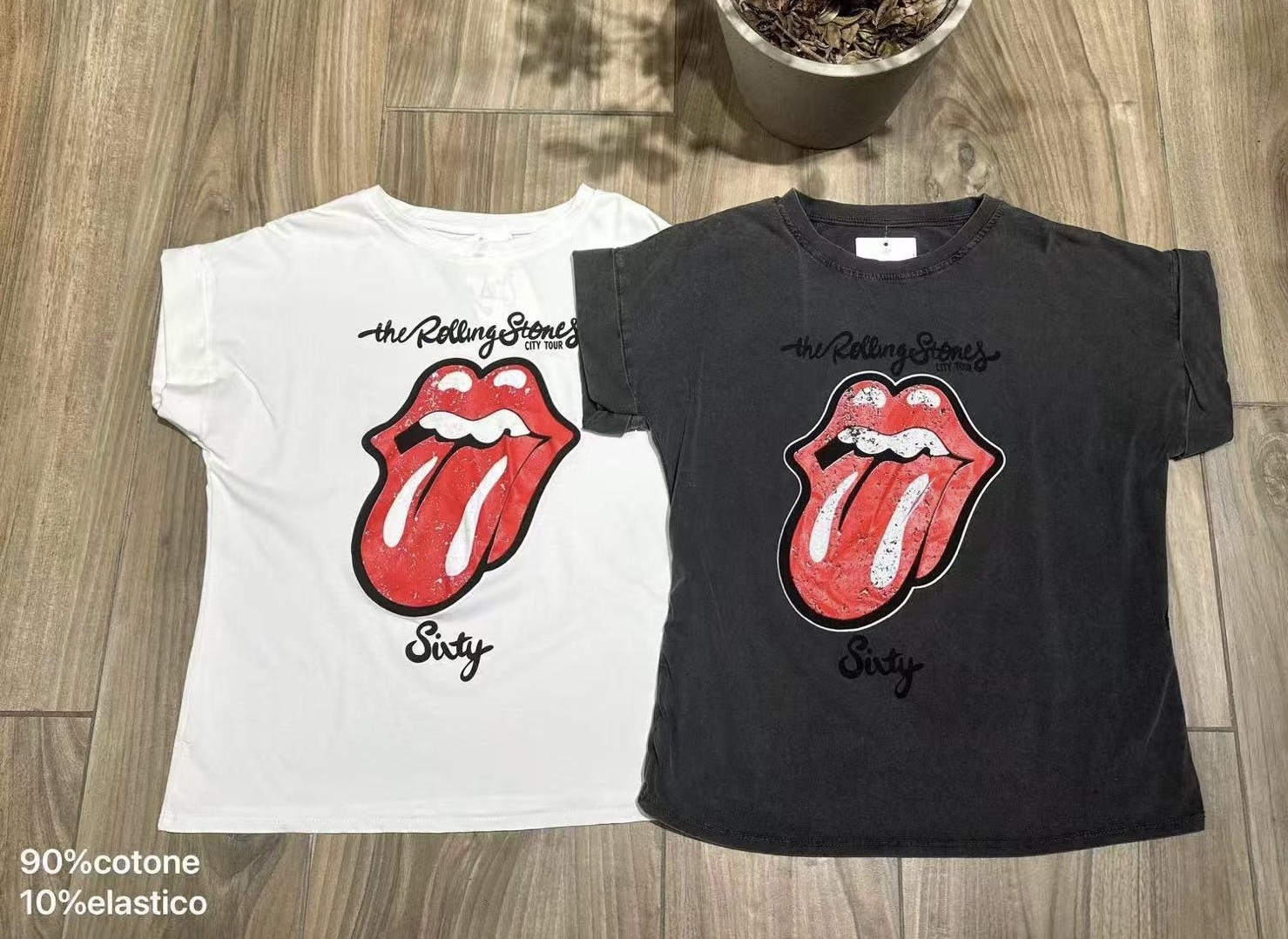 Duas t-shirts The Rolling Stones, branca e preta, com estampa vermelha e preta, em chão de madeira