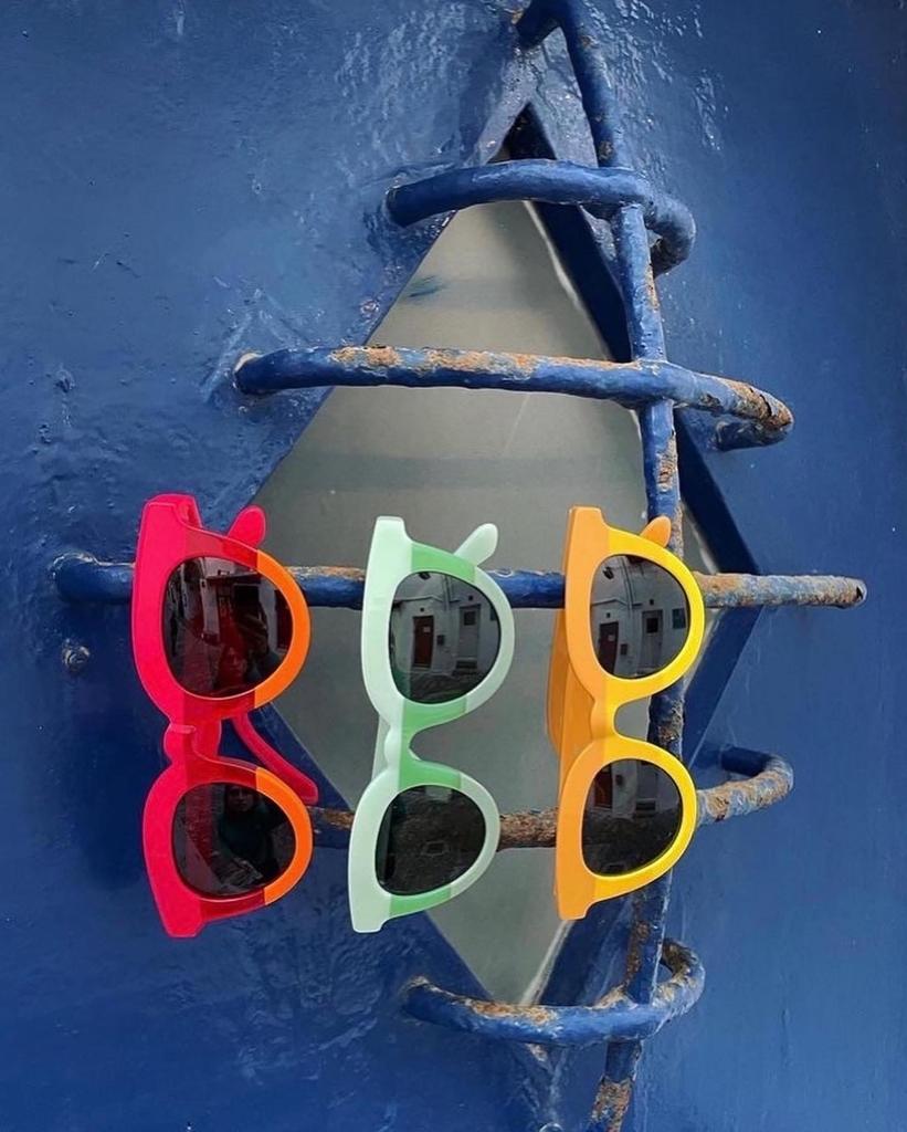 Três óculos de sol coloridos pendurados em grades azuis com ferrugem