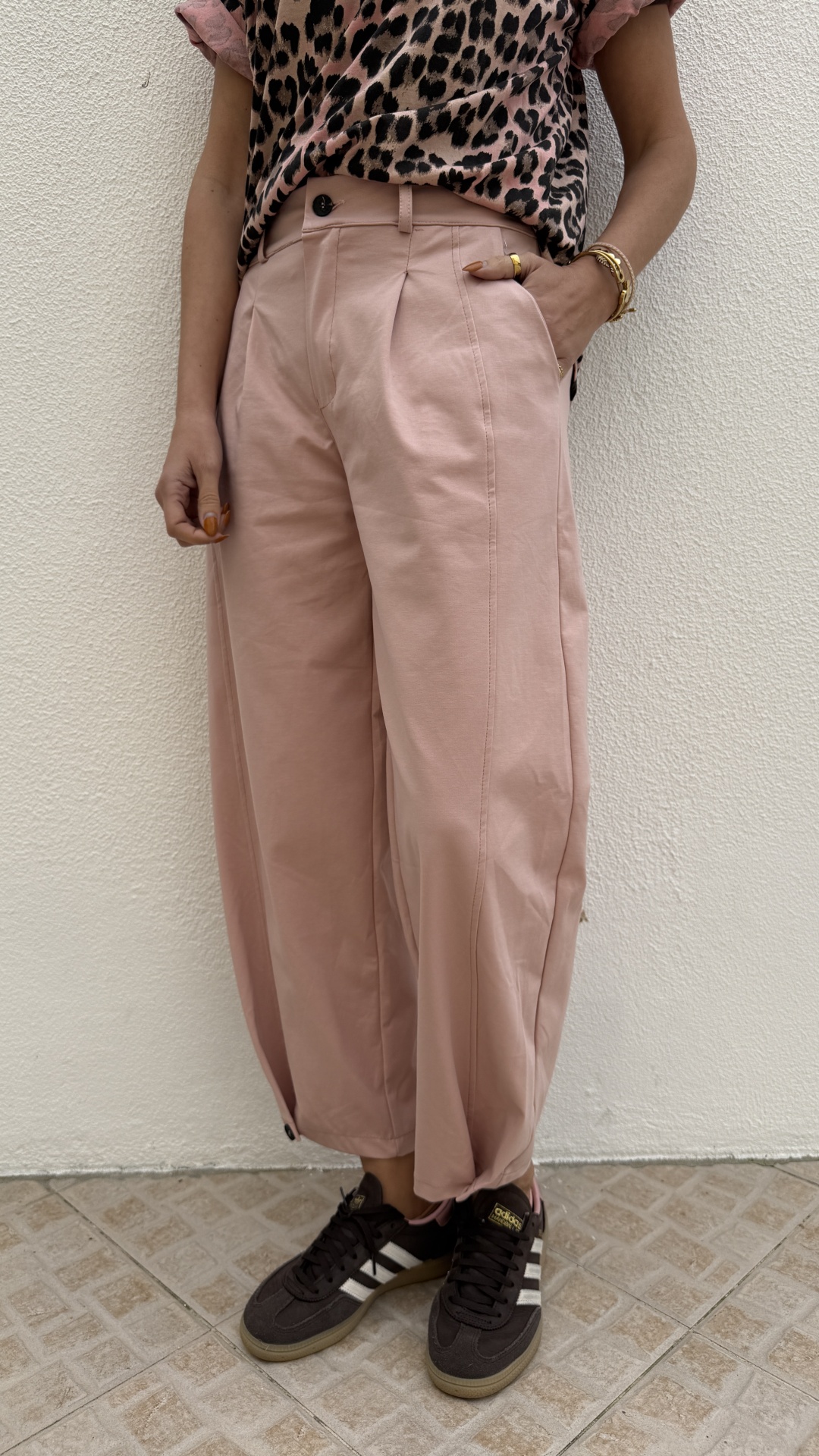 Calças rosas largas com botão preto, t-shirt de padrão onça e sapatilhas Adidas pretas com riscas brancas.