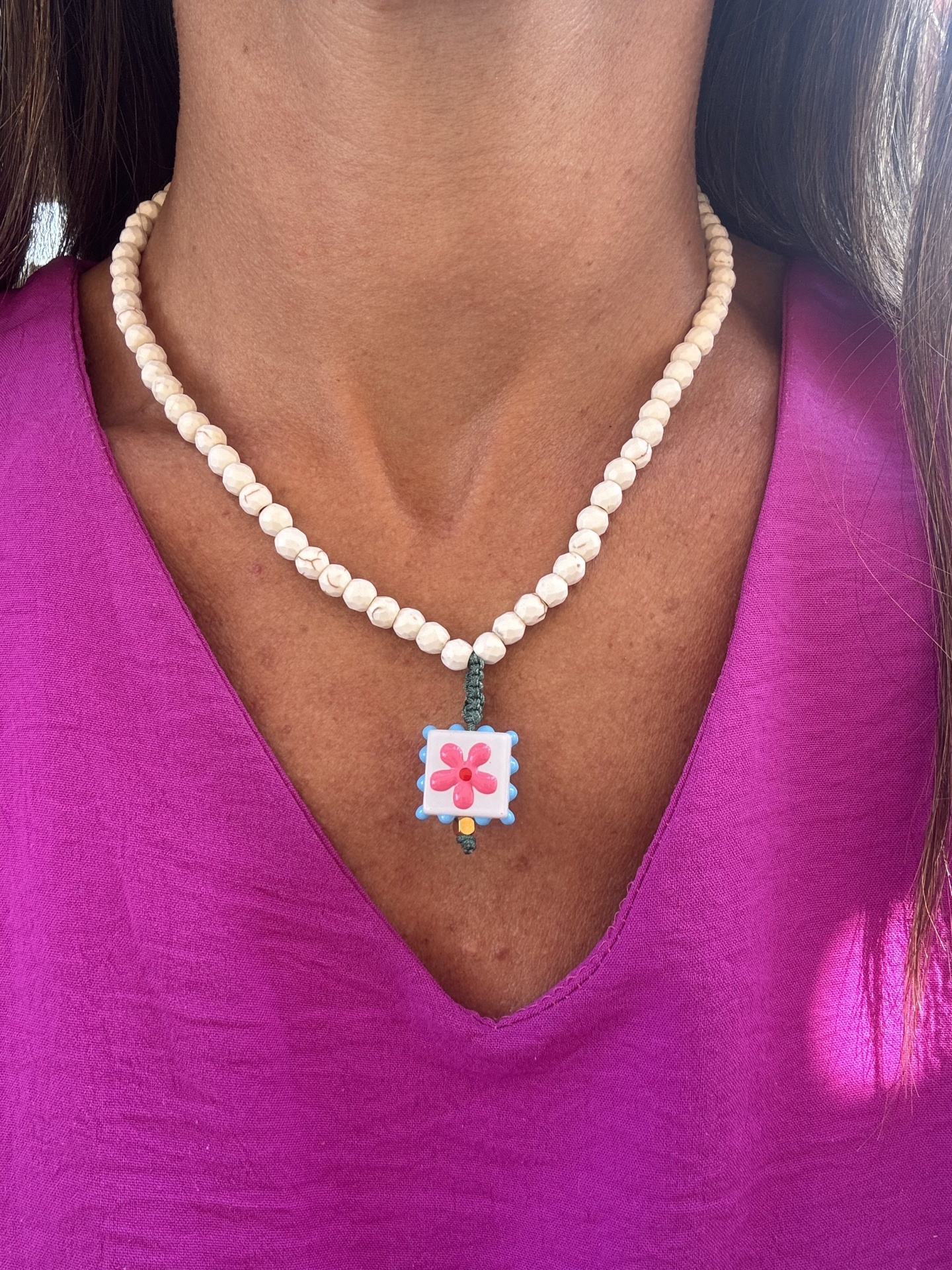 Colar de contas brancas com pendente floral quadrado numa pessoa com blusa roxa