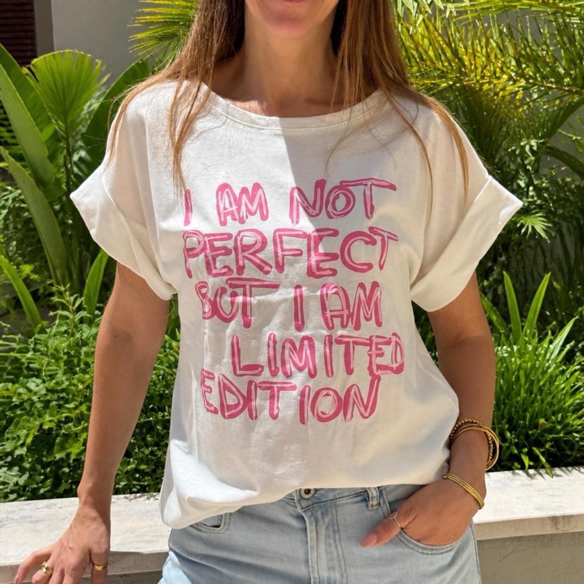 T-shirt branca com texto rosa usada por mulher com jeans claros ao ar livre