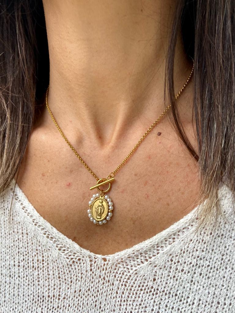 Colar dourado com pendente oval e pérolas em pescoço com camisola branca