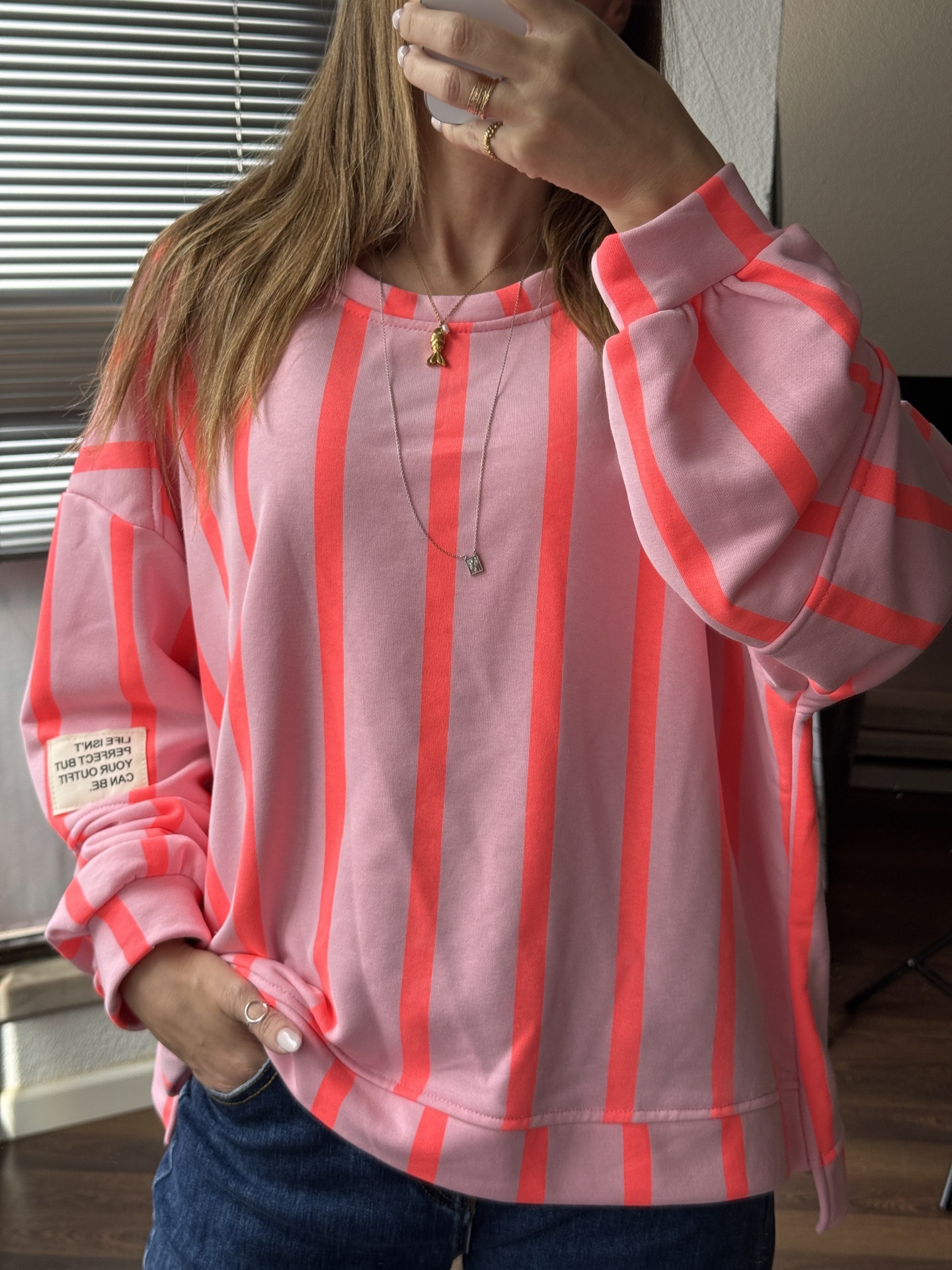 Sweatshirt rosa com riscas verticais fluorescentes e etiqueta na manga usada por pessoa com calças de ganga