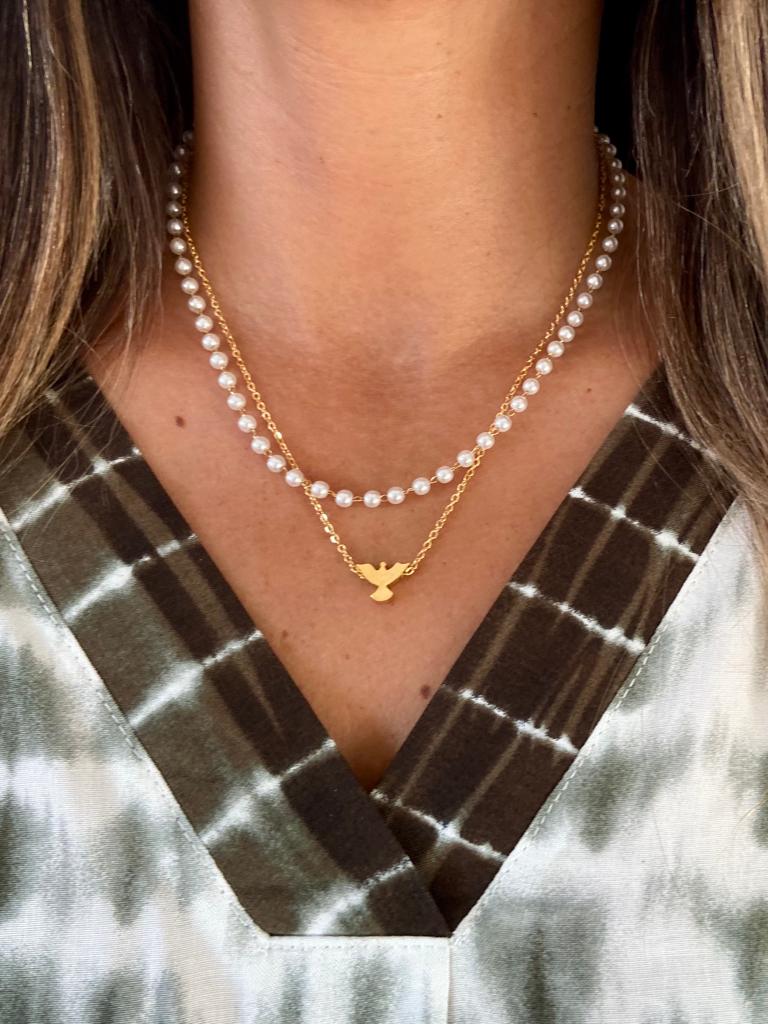 Colar duplo com pérolas e corrente dourada com pendente pá, usado por pessoa com camisa tie-dye