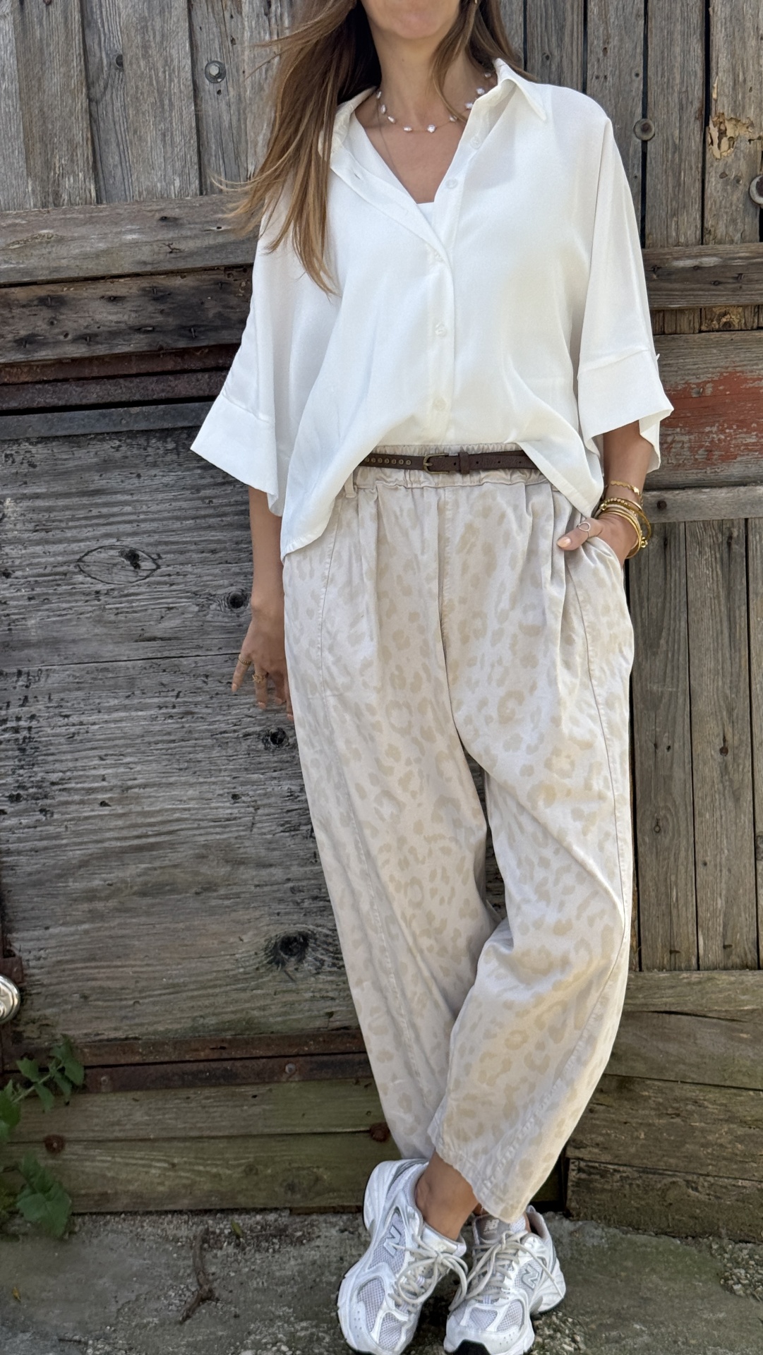 Calças bege com padrão animal, blusa branca, cinto castanho e sapatilhas brancas em frente a porta de madeira