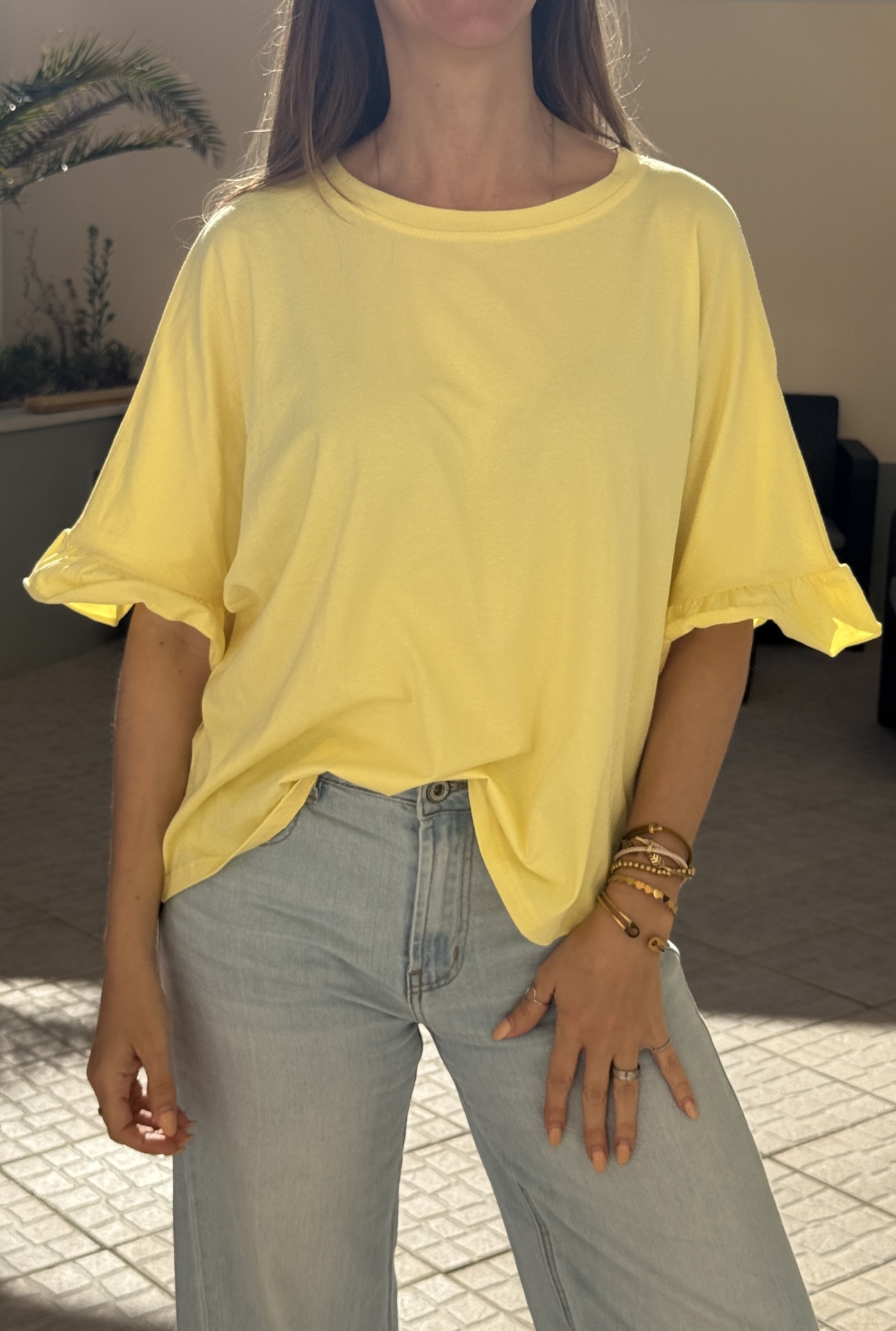 Camisola amarela de manga curta com folhos e jeans claros em ambiente interior