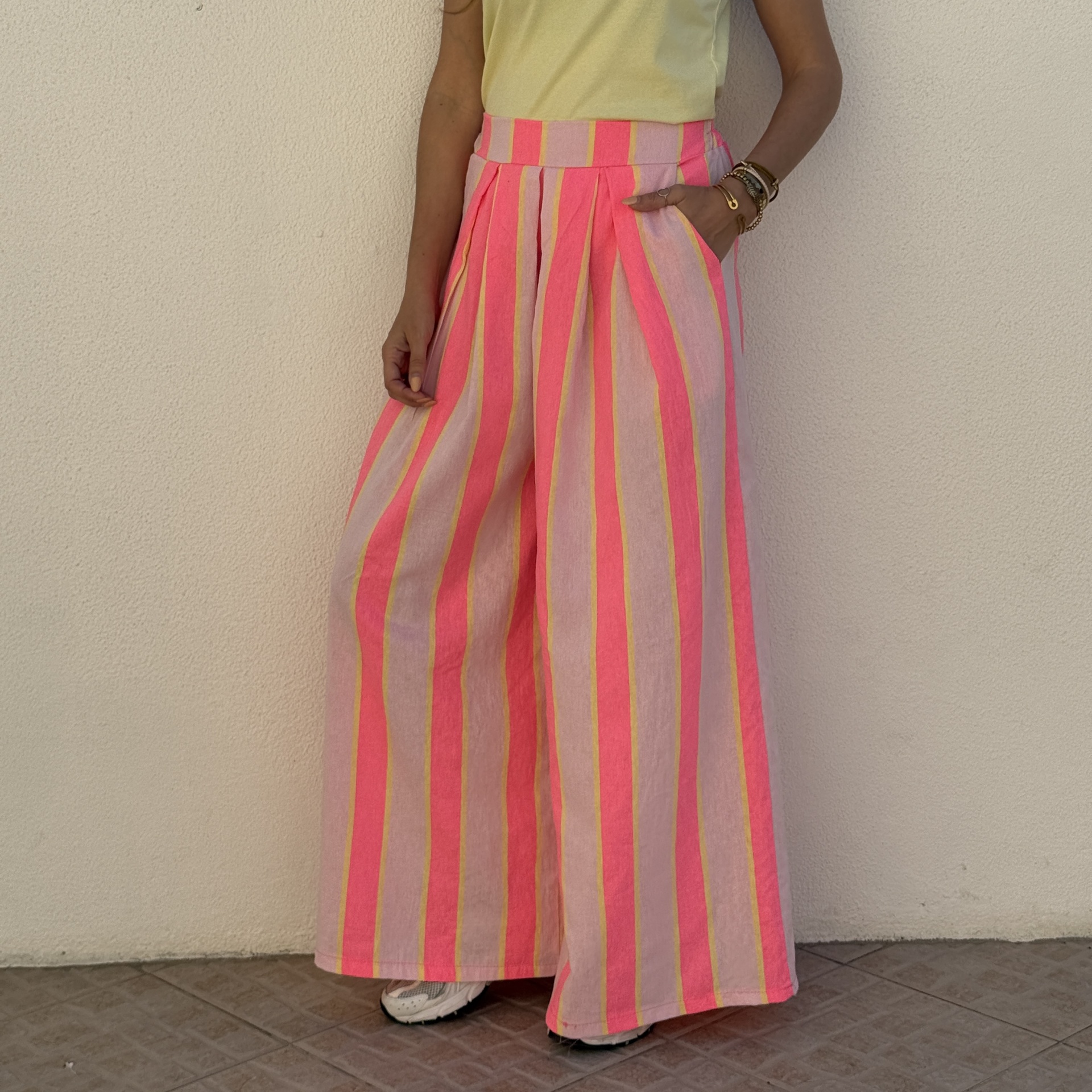 calças largas riscas rosa e amarelas com cintura alta e bolsos, t-shirt amarela, pulseiras douradas e ténis brancos