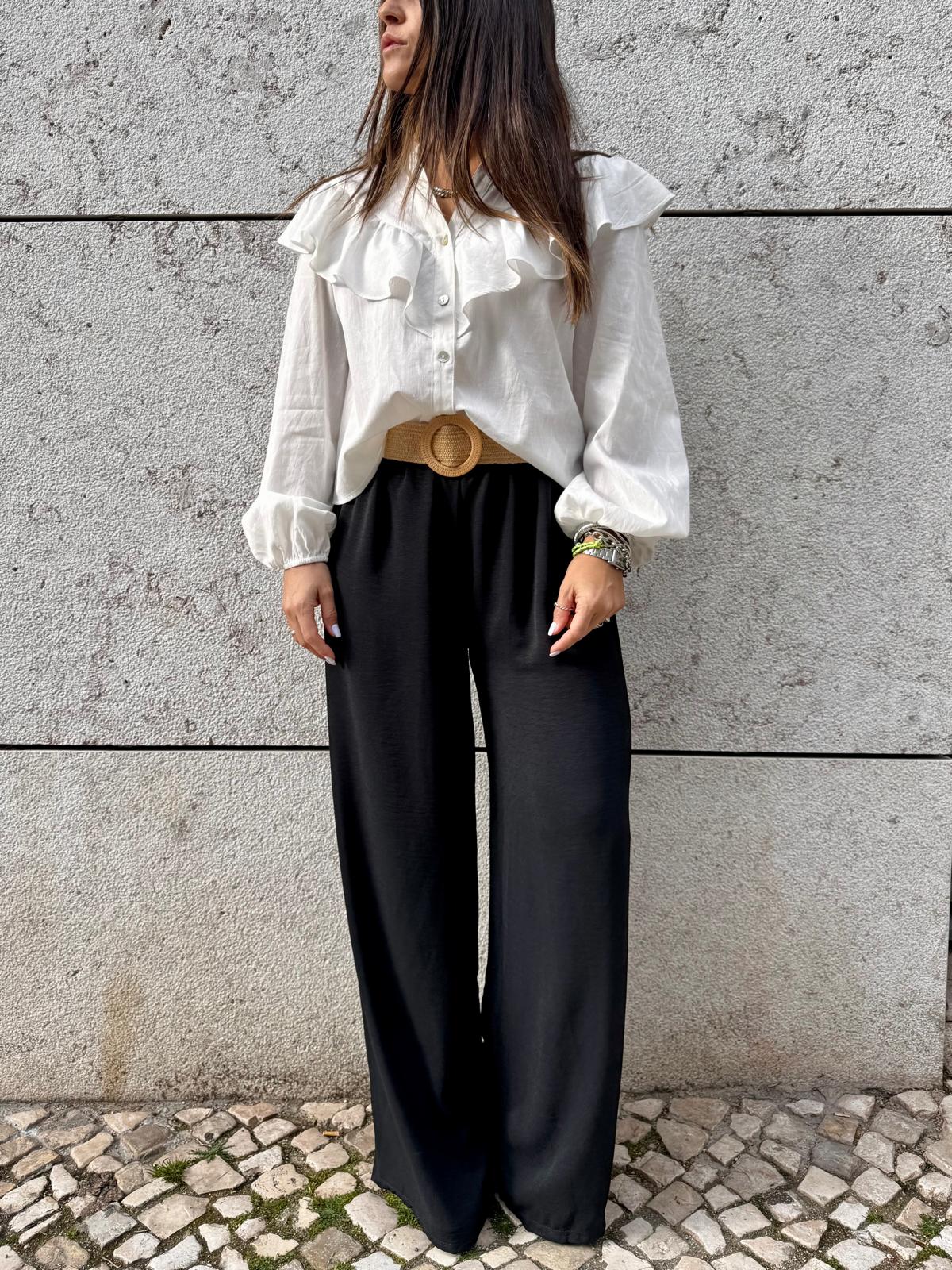 Mulher com blusa branca de folhos e calças pretas largas com cinto castanho de fivela redonda