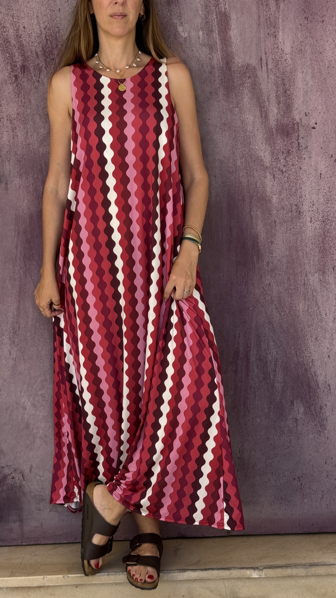 Vestido longo padrão ondulado em vermelho, rosa e branco com sandálias castanhas.