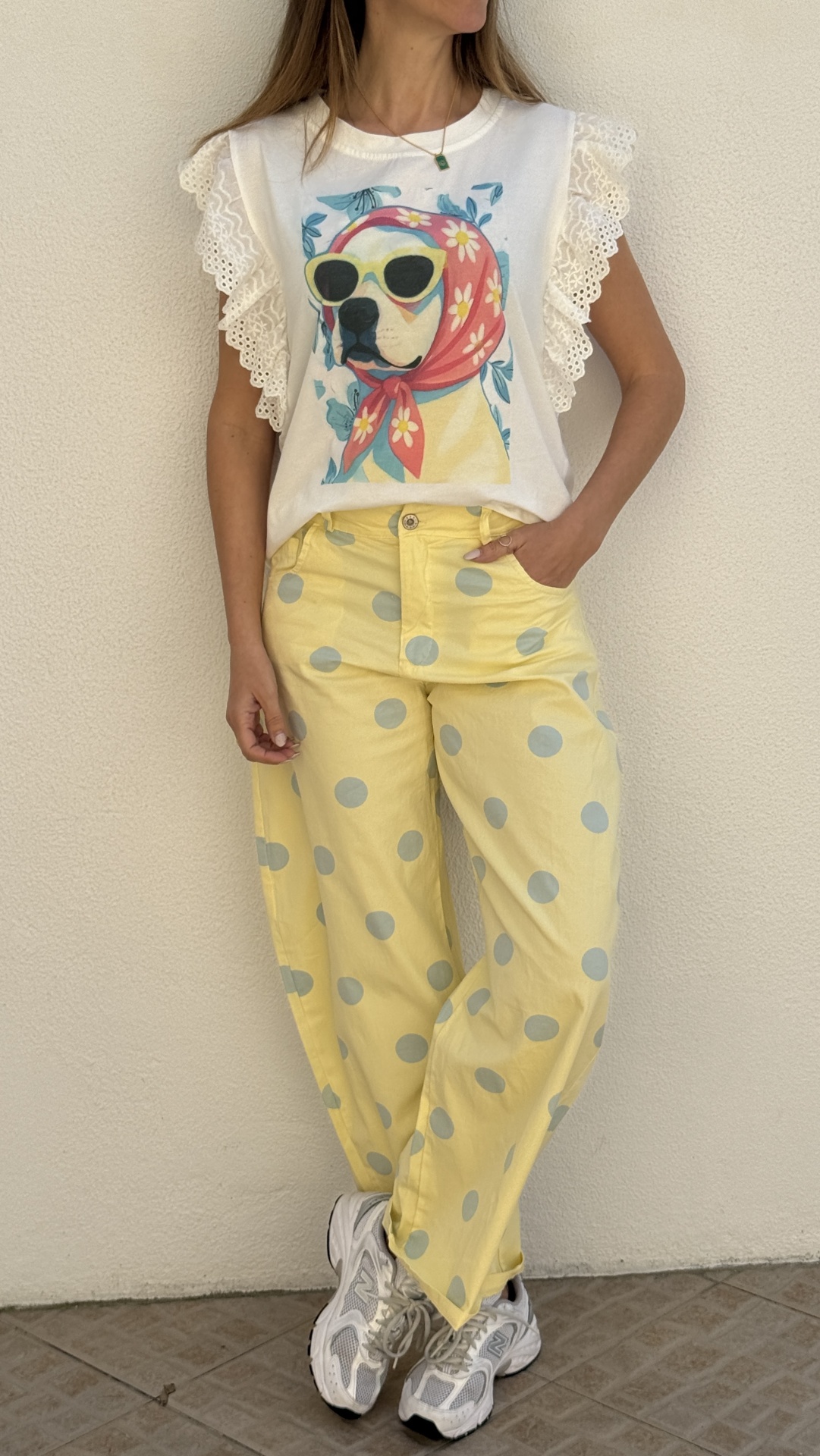 Pessoa com t-shirt branca com estampa de cão, calças amarelas às bolinhas azuis e ténis brancos.