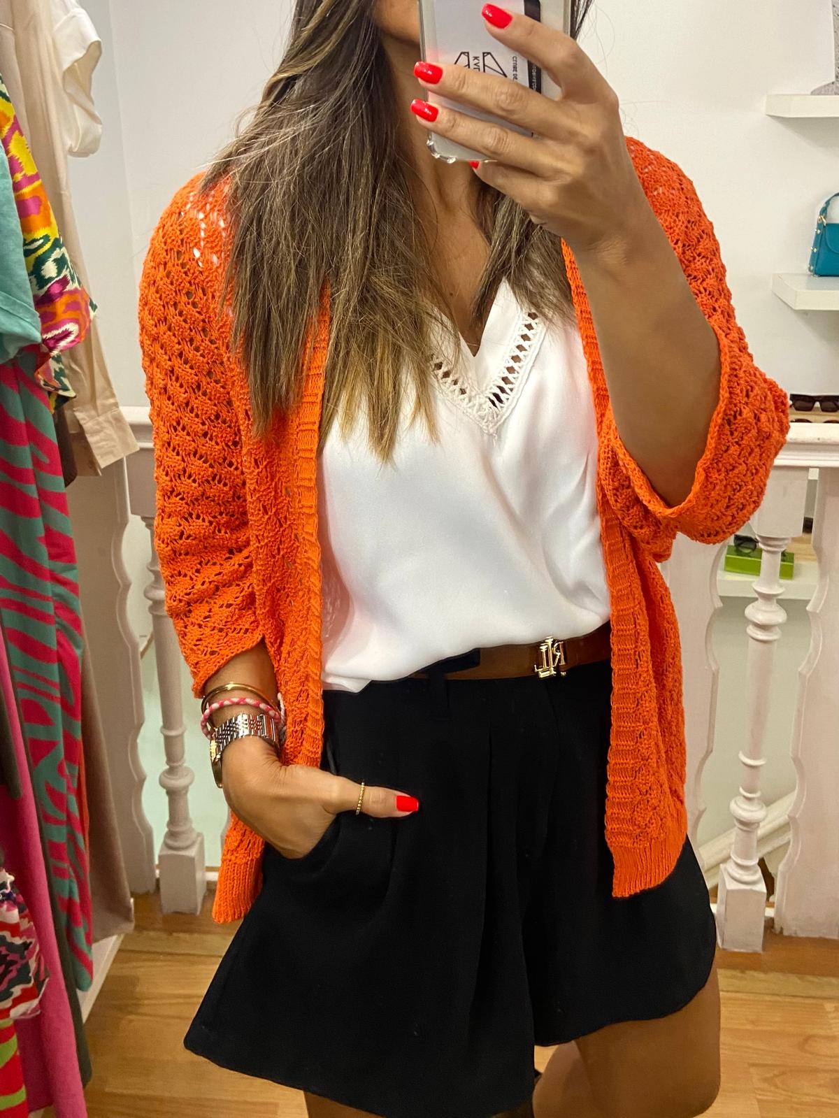 Mulher com cardigan laranja, blusa branca e calções pretos