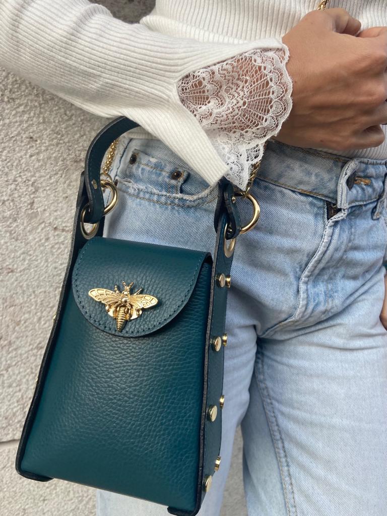 Mala de pele verde escuro com abelha dourada e alça preta ao braço de pessoa