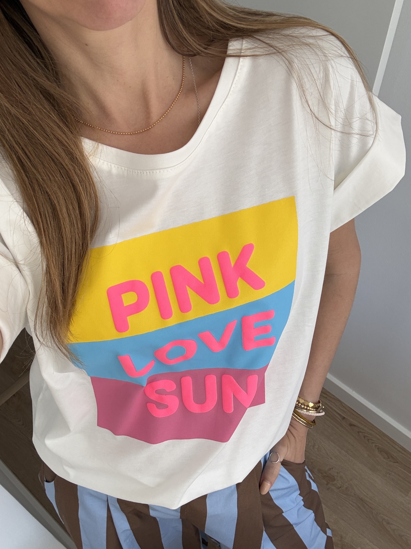 T-shirt branca com estampa colorida e letras cor-de-rosa usada com calças raiadas azuis e castanhas.