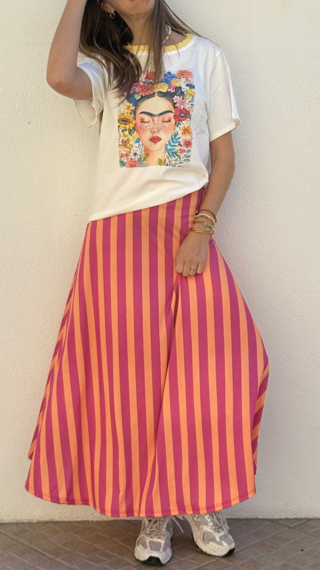 Mulher a usar saia longa rosa e laranja às riscas, t-shirt branca com estampa colorida e ténis cinza e branco