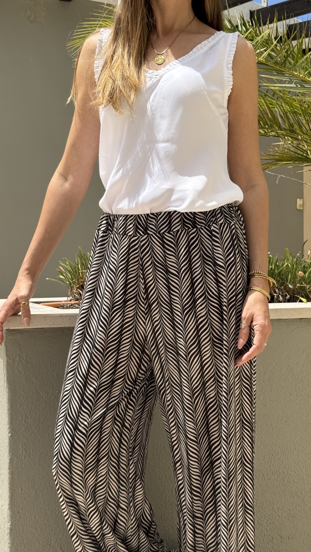 Mulher com blusa branca e calças pretas e brancas com padrão geométrico.