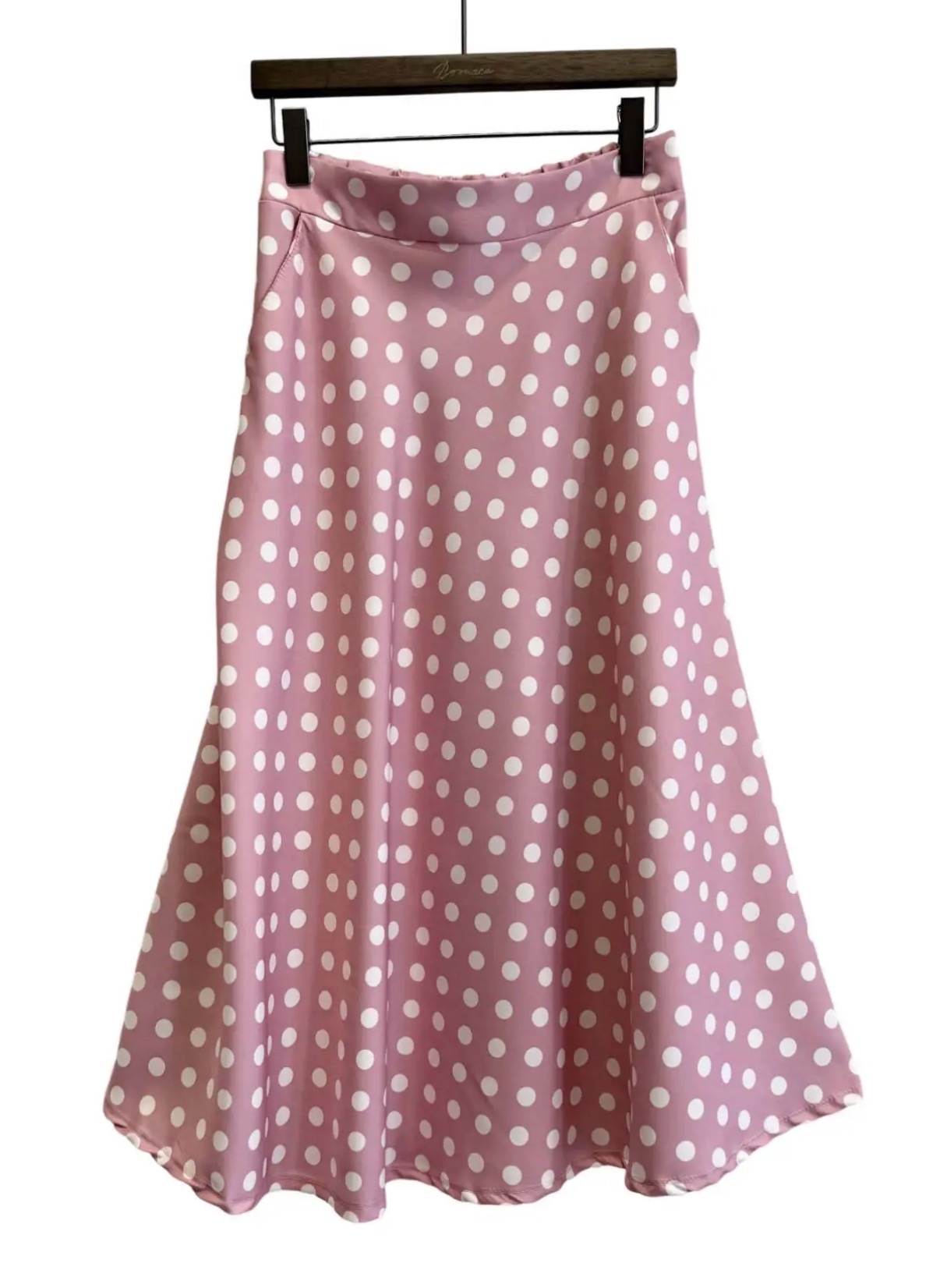 Saia feminina rosa com bolinhas brancas pendurada num cabide.