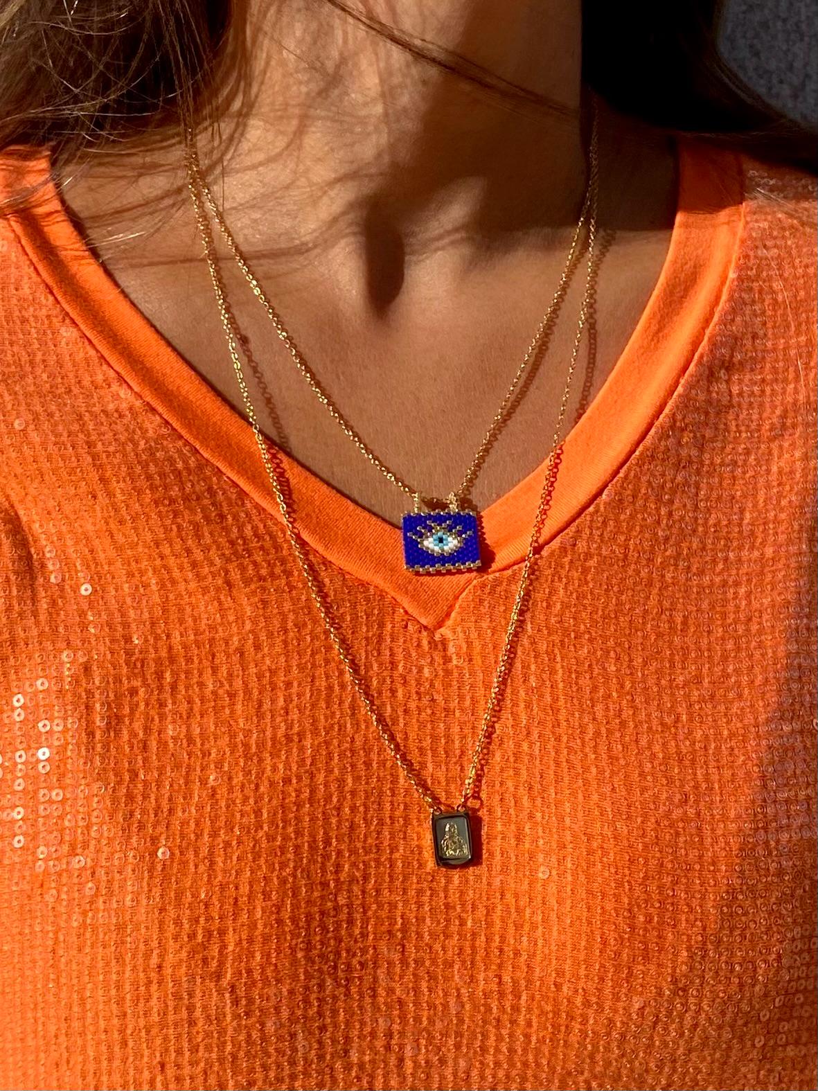 Duas gargantilhas douradas com pingentes sobre roupa laranja texturada e brilhante