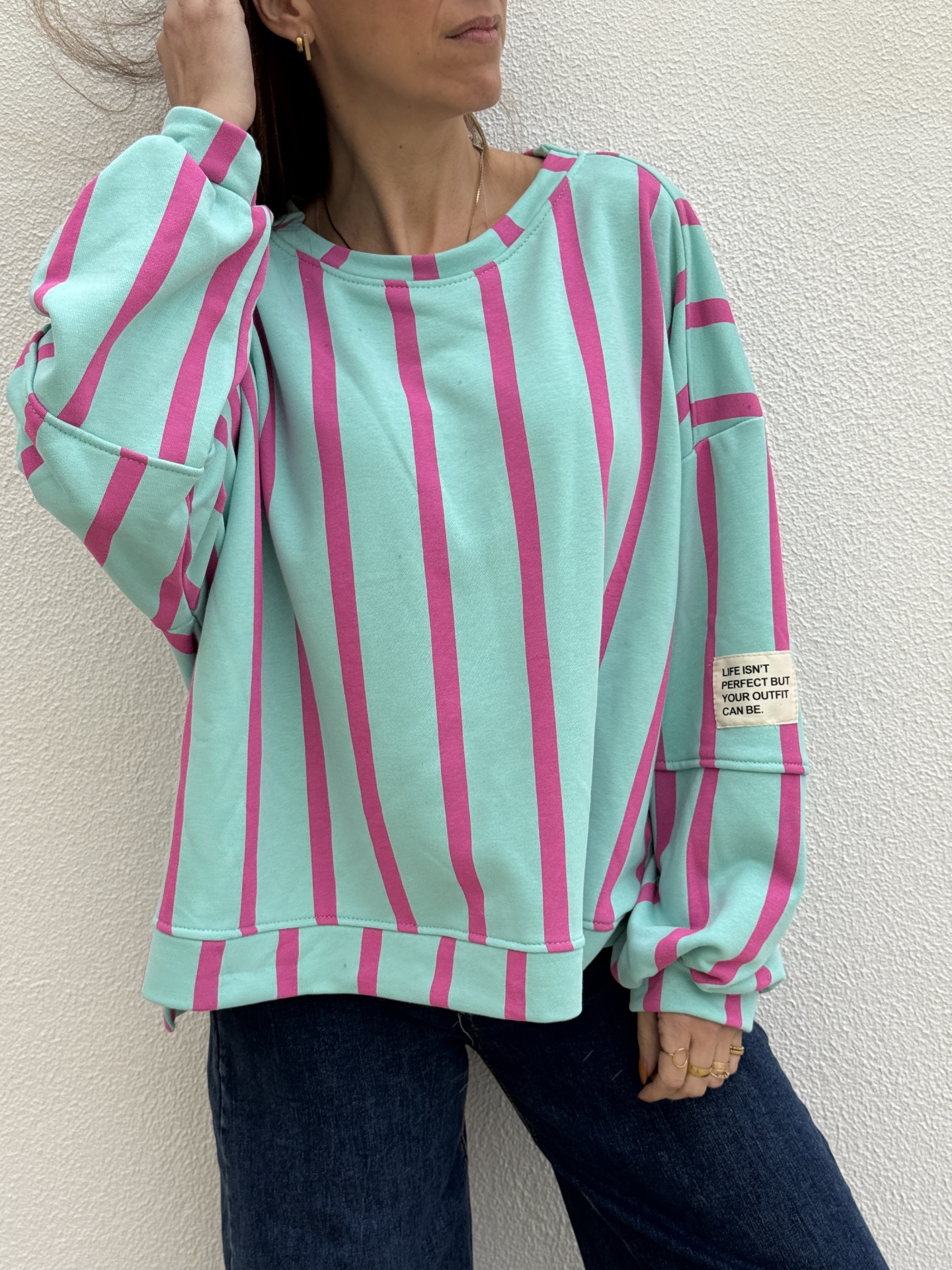Mulher a usar sweatshirt verde água com riscas rosas e calças jeans escuras