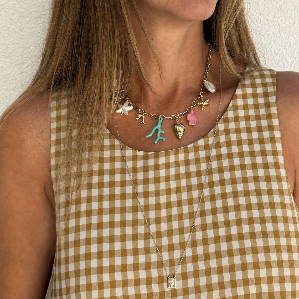 Colar dourado com pendentes coloridos em mulher com vestido xadrez amarelo e branco