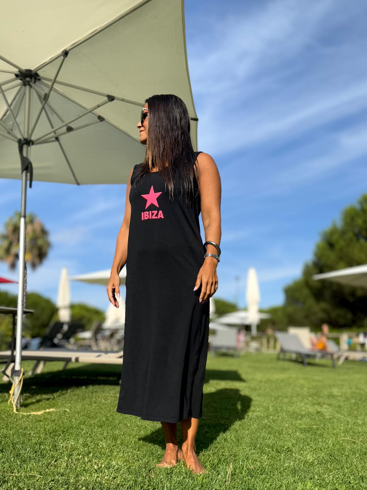 Mulher com vestido longo preto com estrela rosa e texto IBIZA em relvado ao ar livre