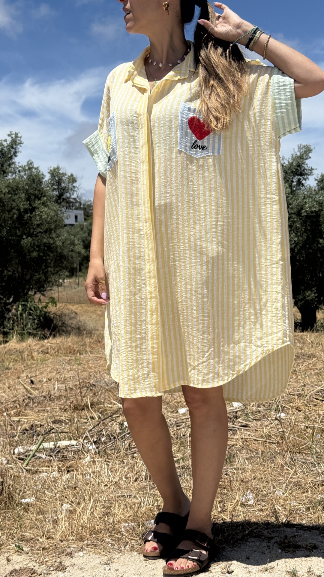 Vestido amarelo claro às riscas com bolso love e sandálias pretas em campo.