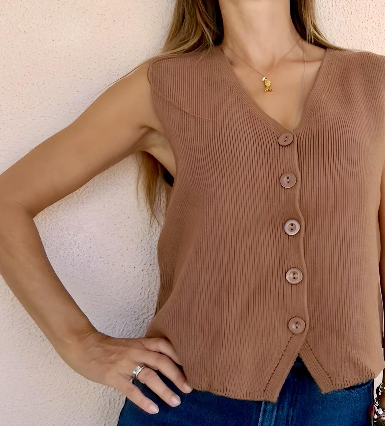 Camisola castanha sem mangas em malha canelada com botões, decote em V, contra parede branca