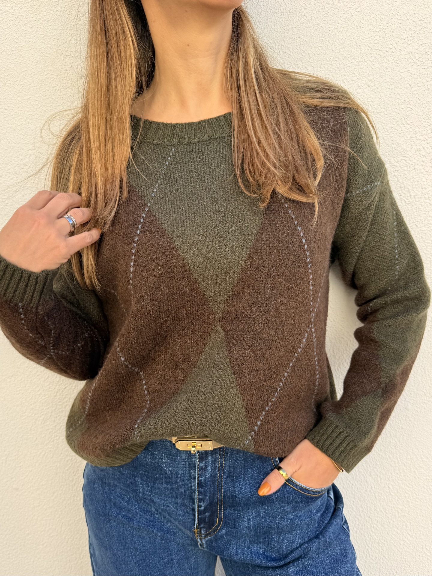 Camisola de malha verde e castanha com padrão de losangos em mulher com jeans azuis