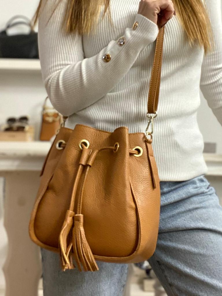 Mala de pele castanha com cordão e tasséis, alça fina, usada com camisola branca e jeans azuis