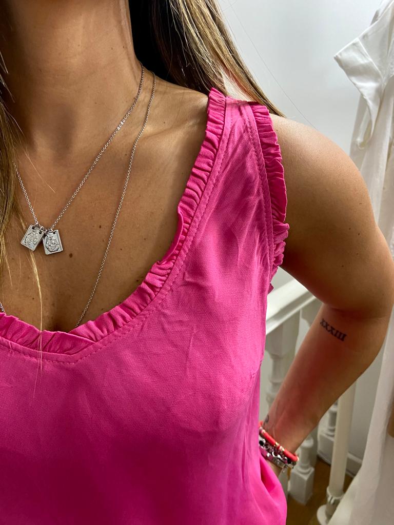 Top rosa com decote em V e borda franzida, colar prateado com pendentes e tatuagem no braço