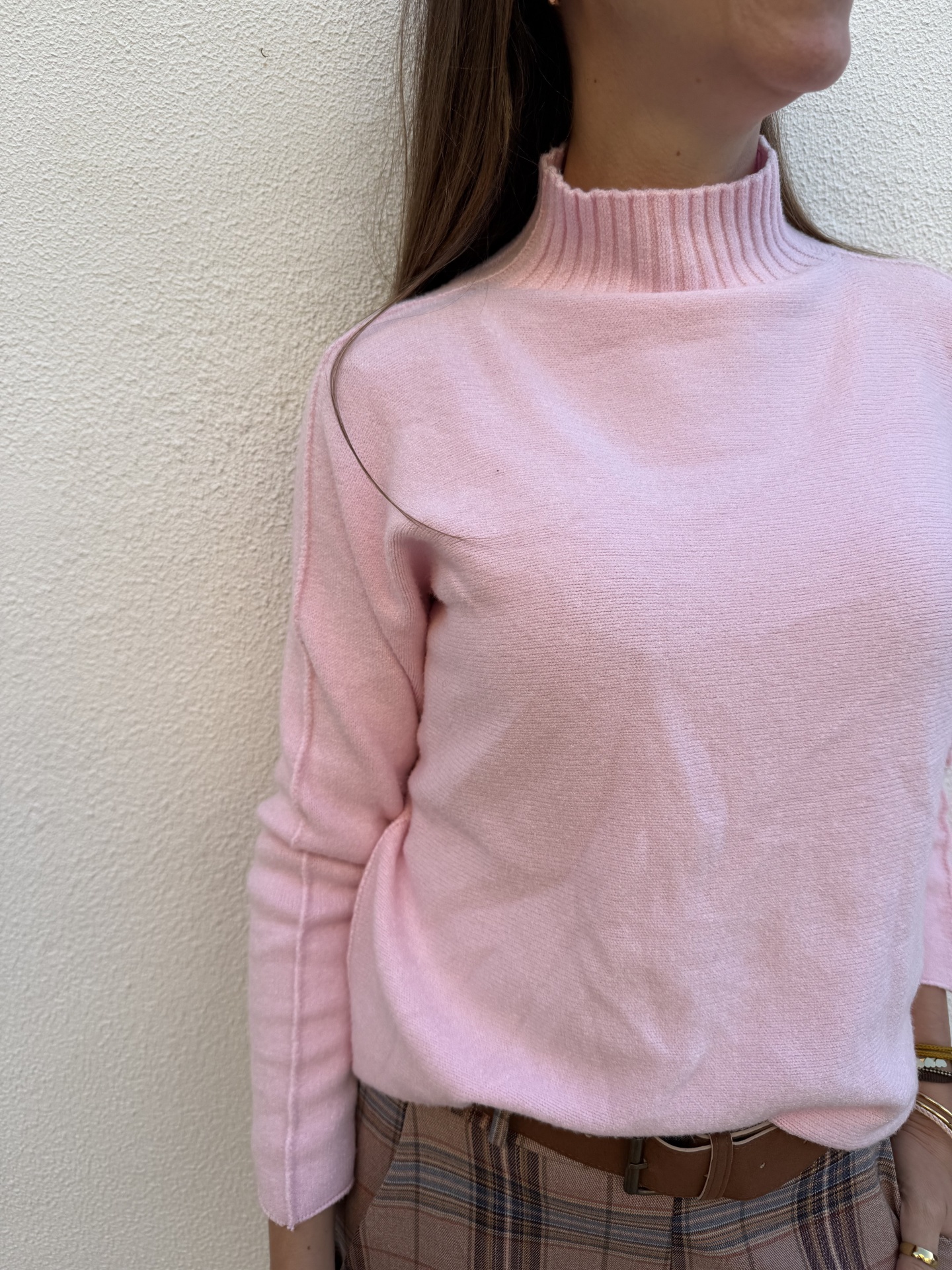 Camisola rosa com gola alta canelada e calças aos quadrados castanhas com cinto castanho.