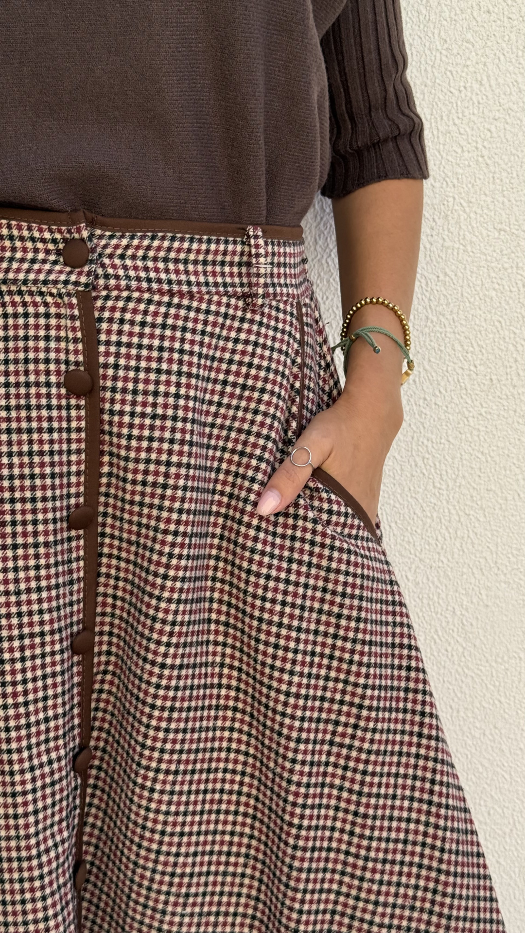 Saia com padrão pied-de-poule em creme, vermelho e preto com botões castanhos e camisola castanha