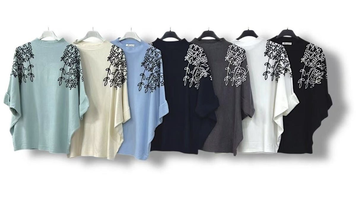 Sete t-shirts coloridas com bordados florais nos ombros penduradas em cabides.