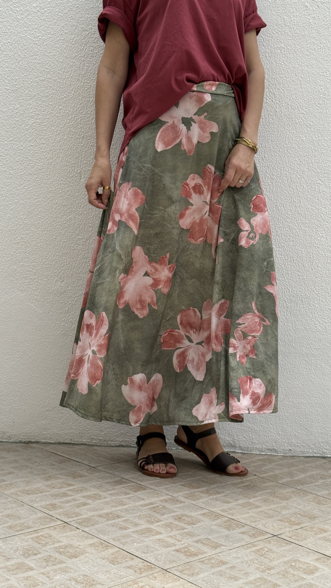Saia longa floral verde com rosas, t-shirt vermelha e sandálias negras.
