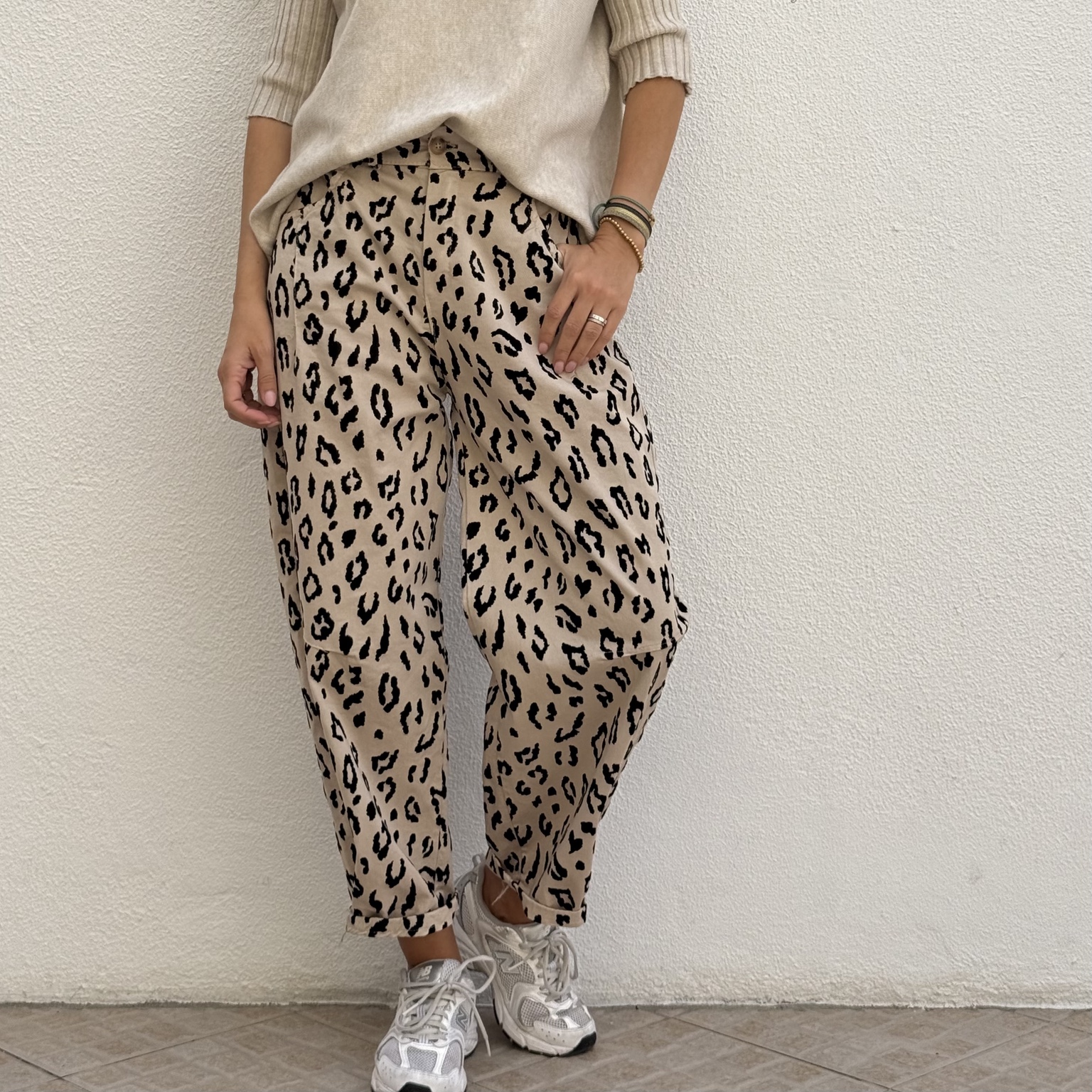 Calças bege com padrão animal print e ténis brancos em chão de azulejo