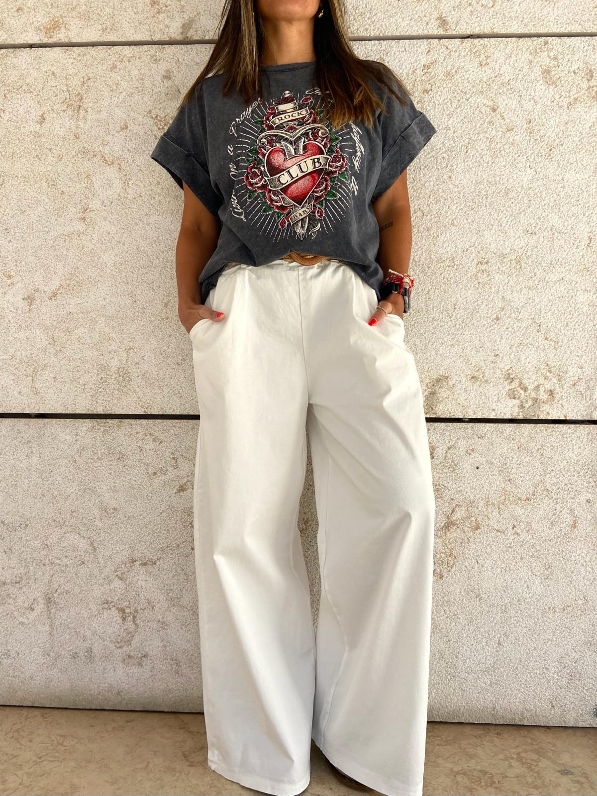 Pessoa com t-shirt preta estampada e calças largas brancas contra parede cinzenta