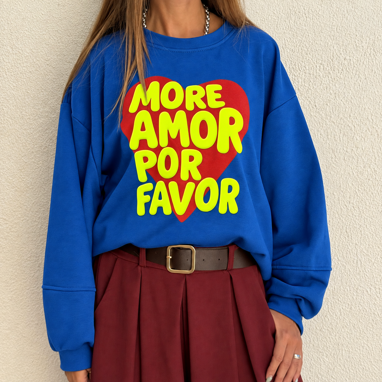 Sweatshirt azul com coração vermelho e texto amarelo, saia castanha plissada e cinto castanho.