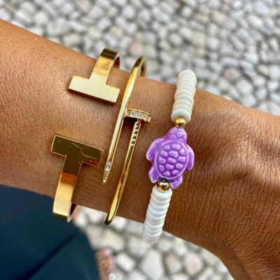 Pulseiras douradas e pulseira com contas brancas e tartaruga roxa no pulso.