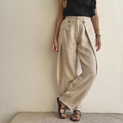 Calças bege e sandálias pretas com tachas usadas por mulher em fundo branco.