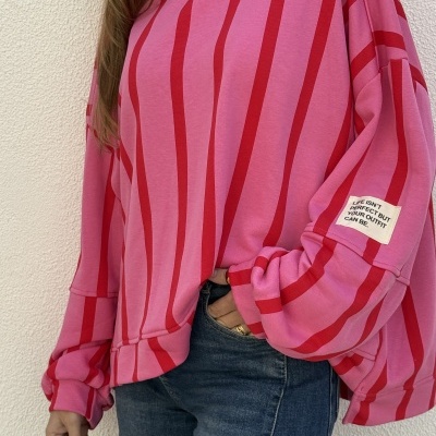 Camisola rosa de riscas vermelhas com etiqueta na manga e jeans azuis.