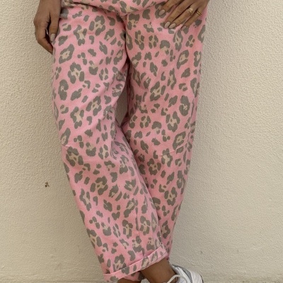 Calças rosa com padrão de leopardo cinza e bege, usadas com sapatilhas brancas em chão de azulejos
