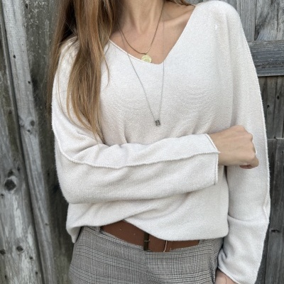 Mulher com camisola creme e calças aos quadrados cinzentas junto a parede de madeira.