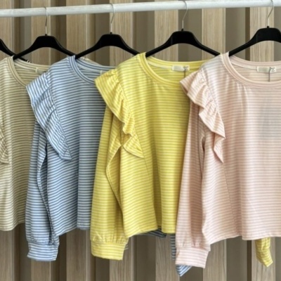 Cinco blusas às riscas com volantes nas mangas, em várias cores, penduradas em cabides pretos