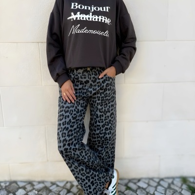 Mulher com camisola preta com texto, calças animal print e sapatos brancos numa calçada portuguesa