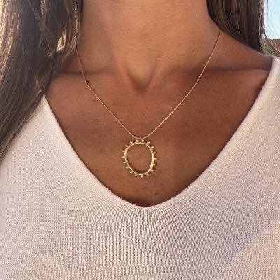 Colar dourado com pendente circular usado ao pescoço sobre camisola rosa clara
