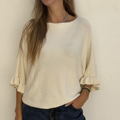 Camisola creme de malha com mangas 3/4 e detalhes franzidos nas mangas, usada com jeans escuros e acessórios no pulso.